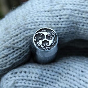 May include: A silver metal stamp with a detailed design of swirling clouds. The stamp is circular and has a raised edge.