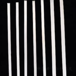 May include: Several thin, white metal strips are displayed vertically against a black backdrop. The strips, of varying widths, appear to be made of a reflective material, possibly silver or a similar alloy. The image has a high-contrast aesthetic.