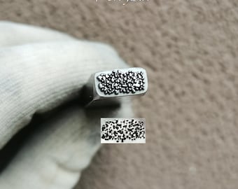 May include: A metal stamping tool with a rectangular head featuring a textured pattern of small, raised, irregular dots. The tool is marked with the text TroyLab and includes a separate rectangular sample imprint showing the dot pattern.