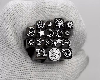 May include: A set of 25 metal stamps featuring celestial and occult symbols. The stamps are arranged in a circle and include images of stars, moons, planets, and a pentagram.