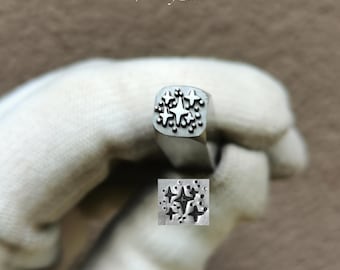 May include: A silver-colored metal stamping tool with a square head featuring a raised design of multiple four-pointed stars and small dots. The tool is marked with the text TroyLab and includes a sample impression showing the star pattern.