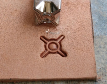 May include: A silver metal leather stamping tool positioned above a tan leather surface. The tool features a four-pointed star design with a central circle, which is clearly impressed into the leather below, accompanied by the text TroyLab.