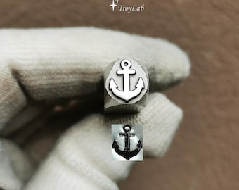 May include: A metal stamping tool featuring a raised anchor design on its face, with the text TroyLab visible above. Below the tool, a black ink impression of the anchor symbol is displayed, showing the clear, detailed nautical shape produced.