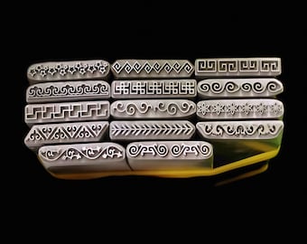 May include: A set of 12 metal stamps with different decorative patterns. The stamps are arranged in a stack, with the top stamp showing a row of stars. The stamps are all silver in color and have black designs.