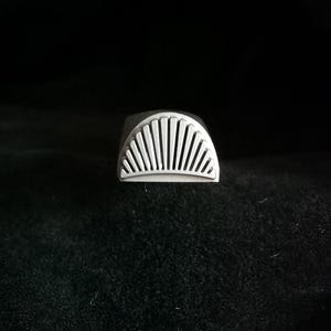Könnte beinhalten: Ein Stempel aus silbernem Metall mit einem Sonnenstrahl-Design. Der Stempel wird verwendet, um Abdrücke in Leder oder anderen Materialien zu erstellen.