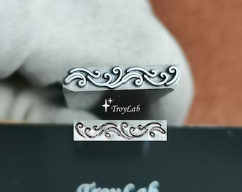 May include: A silver-toned metal stamping tool featuring an intricate, raised scrollwork pattern. The tool displays the text TroyLab. Below the tool, a rectangular impression shows the same detailed, flowing wave-like design in a dark finish.