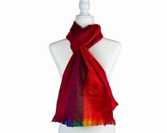 May include: A soft, rectangular scarf featuring a vibrant gradient of colours transitioning from deep red at the top to orange, yellow, green, blue, and purple at the fringed bottom edge. The scarf is draped around a white mannequin torso.