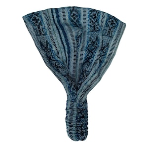 May include: A wide fabric headband featuring a woven pattern in shades of blue, teal, and black. The design includes vertical stripes and repeating geometric diamond motifs. The bottom section is gathered with an elastic band for a secure fit.
