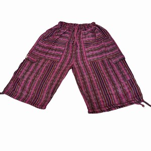 May include: Mid-length shorts featuring a vibrant magenta, purple, and black vertical striped pattern with intricate geometric details. These shorts include an elasticized waistband with a drawstring, two side cargo pockets, and adjustable ties at the leg hems.