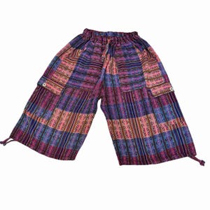 May include: Mid-calf length pants featuring a vibrant patchwork pattern in shades of purple, blue, and pink. The pants have an elasticized drawstring waistband, two large side cargo pockets with button closures, and adjustable drawstring leg hems.