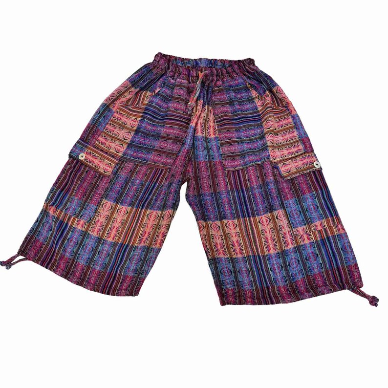 May include: Mid-calf length pants featuring a vibrant patchwork pattern in shades of purple, blue, and pink. The pants have an elasticized drawstring waistband, two large side cargo pockets with button closures, and adjustable drawstring leg hems.