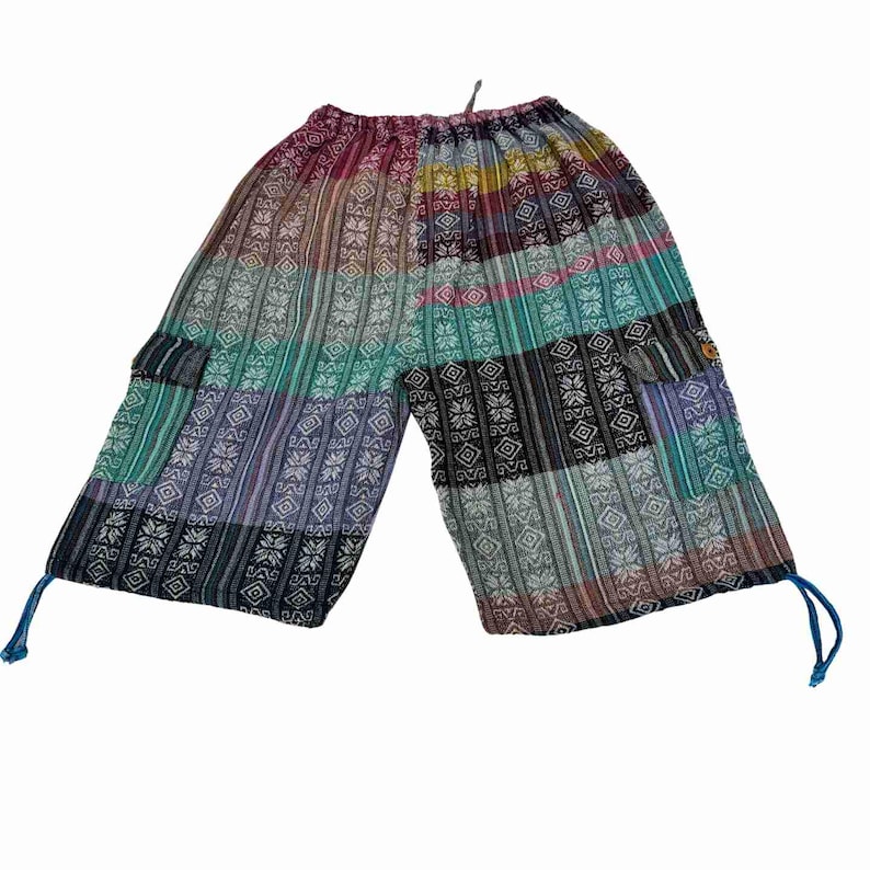 May include: Mid-length pants featuring a patchwork design with vertical stripes and geometric patterns in shades of teal, purple, black, and white. The pants include side cargo pockets, an elastic waistband, and blue drawstring ties at the hems.