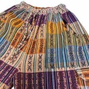 May include: A pair of pants featuring a multicolored woven pattern with vertical stripes in shades of orange, purple, blue, and tan. The garment has an elasticized waistband with a matching fabric drawstring and a visible side cargo pocket.