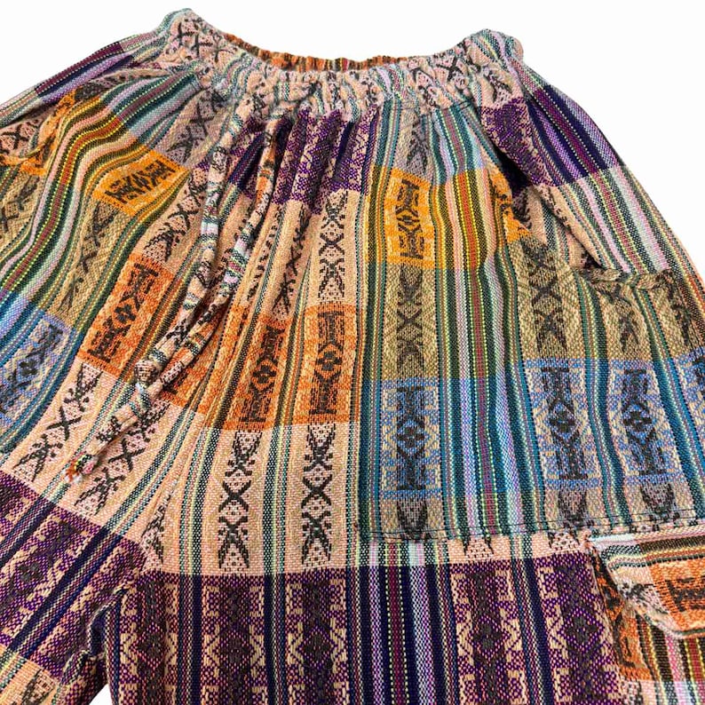 May include: A pair of pants featuring a multicolored woven pattern with vertical stripes in shades of orange, purple, blue, and tan. The garment has an elasticized waistband with a matching fabric drawstring and a visible side cargo pocket.