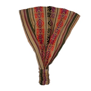 May include: A wide fabric headband featuring a tan base with vertical stripes in orange, purple, and black. The design includes geometric patterns and thin green accents. The bottom section is gathered with an elastic band for a secure fit.