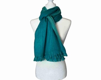 May include: A teal scarf with a fringed edge is draped over a white mannequin. The scarf is a solid colour and appears to be made of a soft material. The scarf is knotted at the neck and hangs down the front of the mannequin.