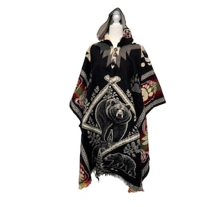 May include: A black hooded poncho featuring a large central graphic of a bear within a diamond-shaped frame, accented by smaller bear motifs, paw prints, and geometric patterns in red, yellow, and white, finished with a two-button front closure.