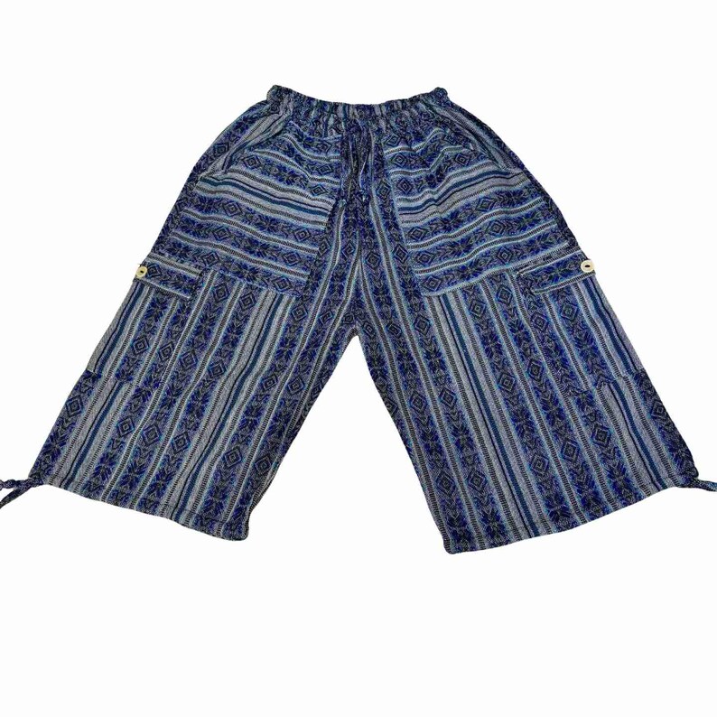 May include: Blue and grey patterned cropped pants featuring a wide-leg silhouette, an elasticized drawstring waistband, and two side cargo pockets with light-colored buttons. The fabric displays alternating vertical stripes and geometric motifs.