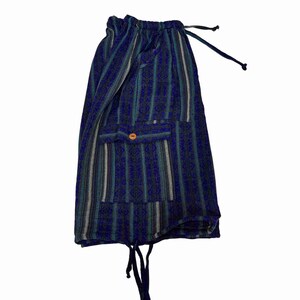 May include: Shorts featuring a vertical striped pattern in shades of dark blue, teal, and grey. The garment includes an elastic waistband with a drawstring, a single patch pocket on the front secured with a small orange button, and a drawstring hem.