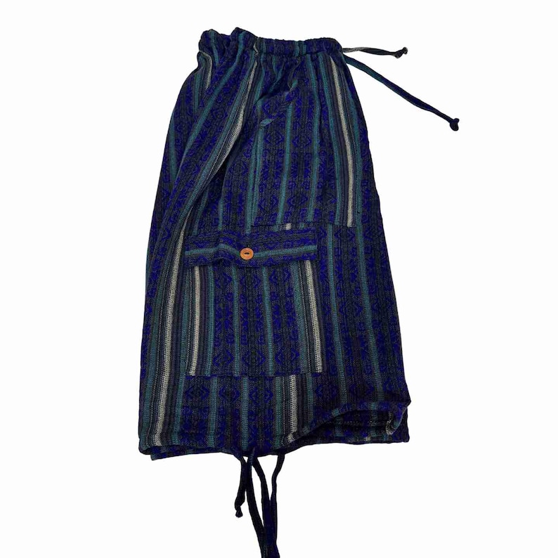 May include: Shorts featuring a vertical striped pattern in shades of dark blue, teal, and grey. The garment includes an elastic waistband with a drawstring, a single patch pocket on the front secured with a small orange button, and a drawstring hem.