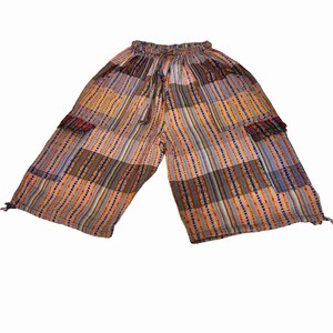 May include: Mid-length pants featuring a patchwork design with vertical stripes in shades of orange, brown, blue, and yellow. The garment includes an elasticized waistband with a drawstring, two side cargo pockets, and adjustable ties at the hems.