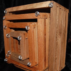 May include: A set of four nesting wooden boxes. The boxes are square-shaped and made of reddish-brown wood. Each box fits inside the next, with the smallest box in the center. The corners are secured with silver wire.