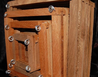 May include: A set of four nesting wooden boxes. The boxes are square-shaped and made of reddish-brown wood. Each box fits inside the next, with the smallest box in the center. The corners are secured with silver wire.