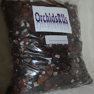 May include: A clear plastic bag filled with orchid potting mix. The mix includes dark brown bark pieces, white and tan stones, and other organic materials. A white label with the text "OrchidsRUs" is visible on the bag.