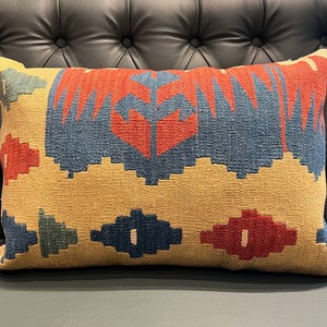 May include: A decorative cushion with a geometric pattern in shades of red, blue, and yellow. The cushion is made of a woven fabric and has a rectangular shape.