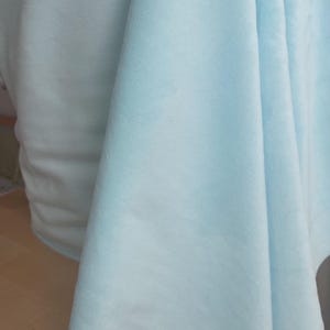 May include: A light blue fabric with a soft, fuzzy texture. The fabric is folded and draped over a surface.