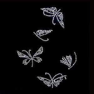 May include: Four white rhinestone butterfly designs on a black background. The butterflies are of varying sizes and are arranged in a random pattern.