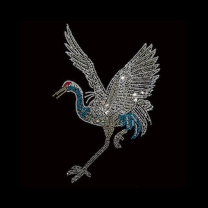 May include: A blue and white rhinestone crane design. The crane is in flight with its wings spread. The crane has a red eye and a long neck.
