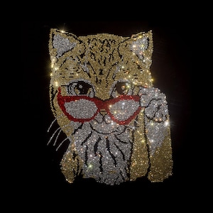 May include: A rhinestone transfer design of a cat face against a black background. The cat is rendered in gold, silver, and white crystals, featuring prominent red-rimmed glasses and a paw raised near its face, creating a sparkling effect.