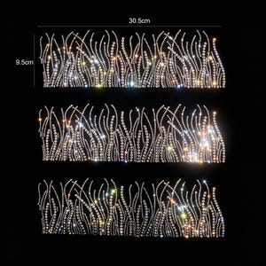 Peut inclure: Trois écussons rectangulaires en strass avec un motif ondulé rappelant de l'herbe, composé de cristaux transparents sur fond noir. Chaque écusson mesure 30,5 cm de largeur et 9,5 cm de hauteur, avec une texture de surface brillante et réfléchissante.