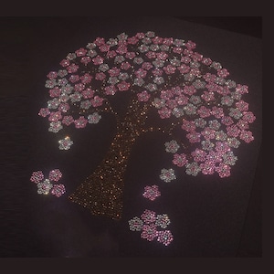 May include: A sparkly pink and white tree made of rhinestones. The tree is on a black background and has a brown trunk. The tree is decorated with small pink and white flowers.