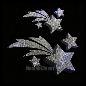 May include: Two sets of silver shooting star appliques covered in reflective rhinestones. Each set features a large five-pointed star with a trailing tail and a smaller detached star. The text NextClover is visible in grey at the bottom center.