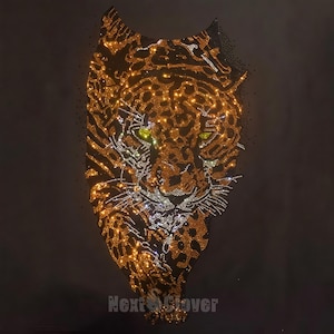 May include: A black fabric surface featuring a large, detailed leopard head design created with shimmering gold, bronze, and silver rhinestones. The leopard has piercing lime green eyes and whiskers. The text Next Clover is printed at the bottom.