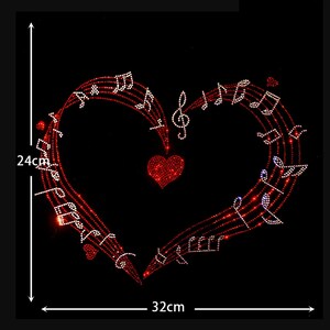 May include: A rhinestone transfer design featuring a heart shape formed by red musical staff lines and white musical notes. A solid red heart sits in the center. The design measures 24 cm in height and 32 cm in width against a black background.