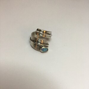 May include: A silver ring with a swirling design and a small, oval-shaped opal gemstone.
