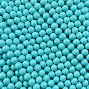 May include: A handful of turquoise-colored round beads. The beads are strung together, creating a dense, textured surface. The beads are a consistent size and shape, and the color is a vibrant, solid turquoise. The beads are held in a hand, with green foliage in the background.