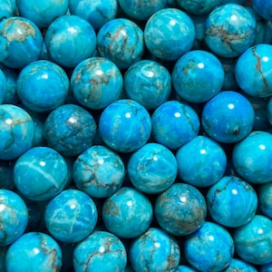 May include: A handful of round, turquoise beads with a marbled appearance. The beads are a vibrant blue-green color with darker, mottled patterns. The beads are likely for jewelry making or crafting.
