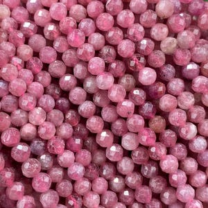 May include: A large collection of small, round, faceted pink tourmaline beads strung together. The beads exhibit varying shades of deep magenta and rose pink with a reflective, polished surface texture, creating a dense, uniform cluster of gemstone spheres.