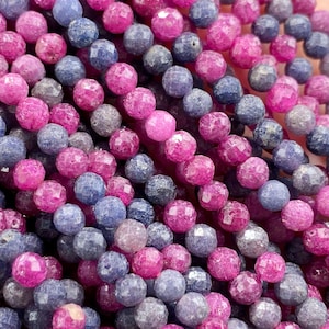 Pode incluir: Uma coleção de pequenas contas redondas facetadas em tons vibrantes de rosa magenta e azul ardósia profundo. As contas estão dispostas em vários fios, exibindo uma superfície texturizada e reflexiva que capta a luz em todo o conjunto.