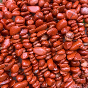 Puede incluir: Un puñado de chips de piedras preciosas de jaspe pulido, de color marrón rojizo. Las piedras varían en tamaño y forma, con un acabado liso y brillante. Las virutas están ensartadas, lo que sugiere que podrían usarse para joyería o manualidades.