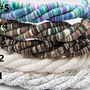May include: Five strands of colorful round beads, stacked on top of each other. The beads are made of different materials, including wood, plastic, and shell. The top strand is a mix of purple, blue, and green beads. The second strand is a mix of brown, green, and white beads. The third strand is a mix of brown and black beads. The fourth strand is white with a subtle speckled pattern. The bottom strand is white with a black speckled pattern. The strands are labeled with numbers 1 through 5.