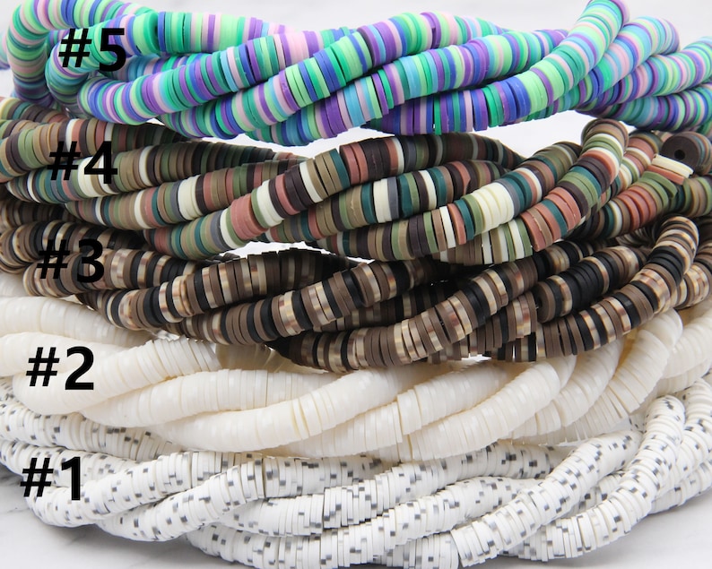 May include: Five strands of colorful round beads, stacked on top of each other. The beads are made of different materials, including wood, plastic, and shell. The top strand is a mix of purple, blue, and green beads. The second strand is a mix of brown, green, and white beads. The third strand is a mix of brown and black beads. The fourth strand is white with a subtle speckled pattern. The bottom strand is white with a black speckled pattern. The strands are labeled with numbers 1 through 5.
