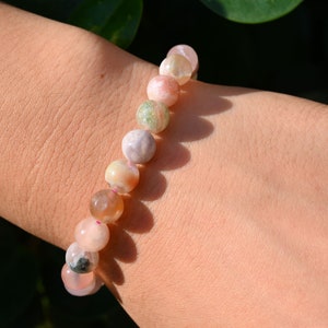 May include: A bracelet made of pink, white, and green agate beads. The beads are round and have a natural, polished finish.