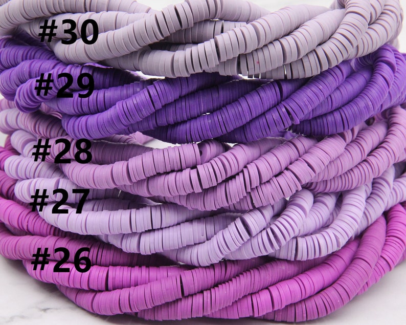 May include: A close-up of a stack of purple and lavender colored polymer clay beads. The beads are arranged in a gradient from light lavender to dark purple. The beads are labeled with numbers 26 through 30.