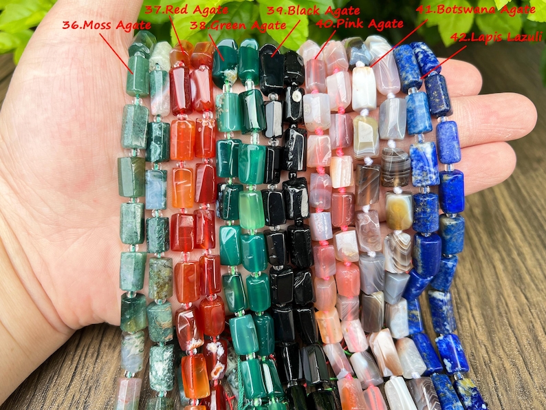 May include: Strands of gemstone beads in various colors, including green moss agate, red agate, green agate, black agate, pink agate, Botswana agate, and lapis lazuli. The beads are rectangular and strung together, showcasing a range of natural stone textures and hues.