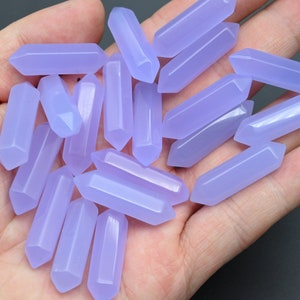 Könnte beinhalten: Eine Sammlung von blass-lavendelfarbenen Kristallspitzen, auch bekannt als Zauberstäbe, in verschiedenen Größen. Die Spitzen sind glatt und poliert und haben ein durchscheinendes Aussehen.